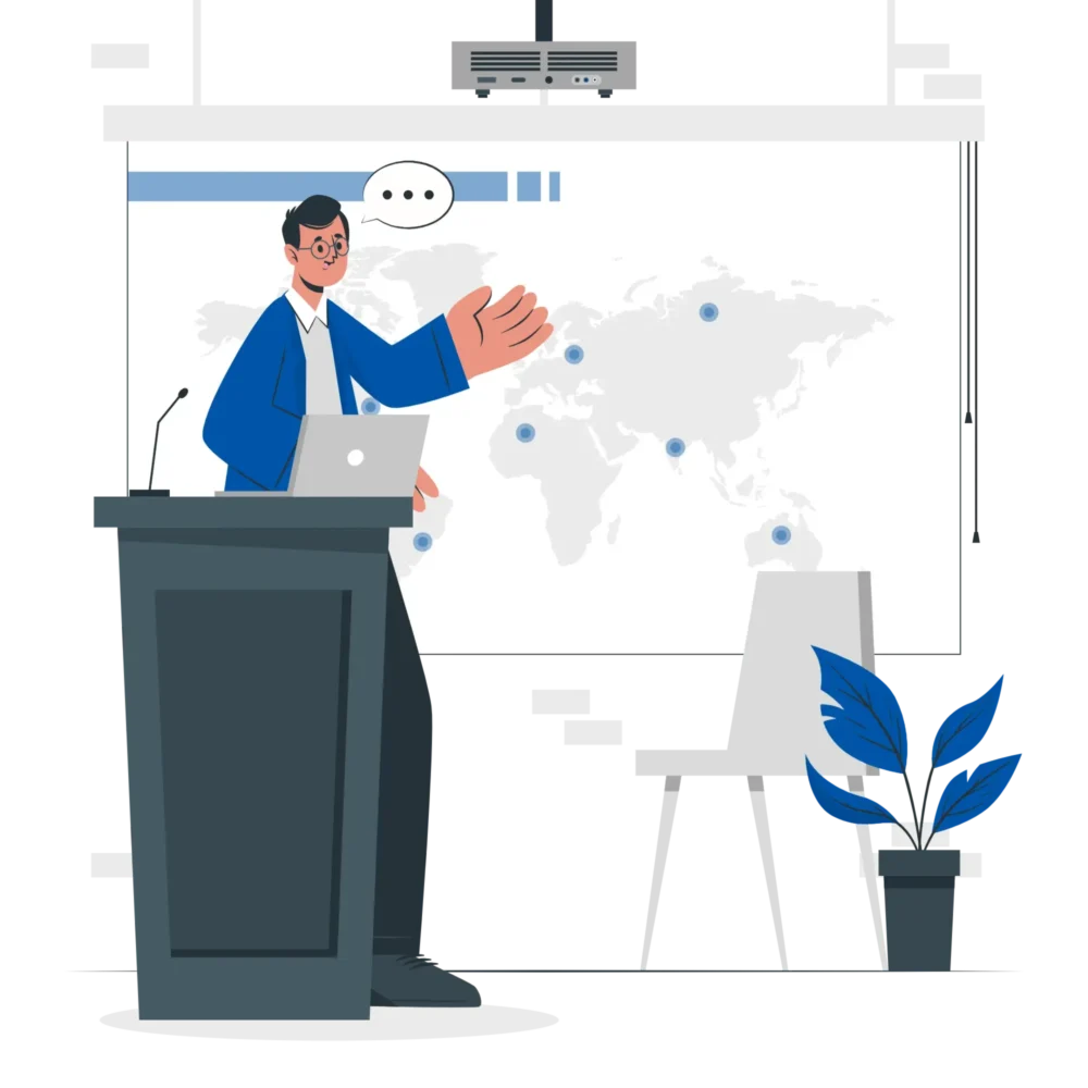 A presenter in a blue jacket gestures towards a world map on a screen, with a laptop on the podium and a plant nearby.